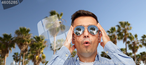 Image of surprised man in sunglasses over palm trees