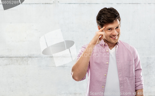 Image of smiling young man pointing finger to his head