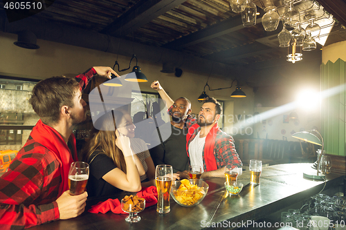 Image of Sport fans cheering at bar, pub and drinking beer while championship, competition is going