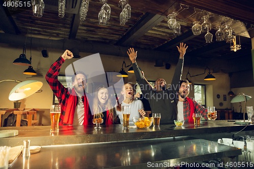 Image of Sport fans cheering at bar, pub and drinking beer while championship, competition is going