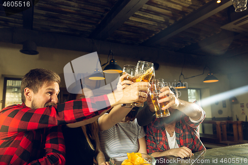 Image of Sport fans cheering at bar, pub and drinking beer while championship, competition is going