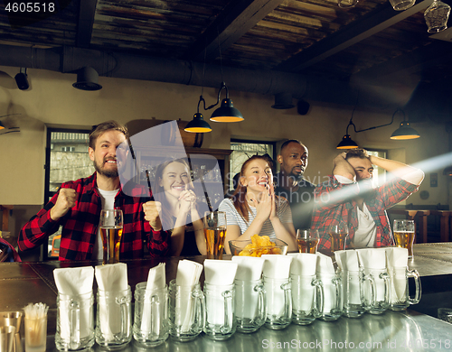 Image of Sport fans cheering at bar, pub and drinking beer while championship, competition is going