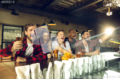 Image of Sport fans cheering at bar, pub and drinking beer while championship, competition is going