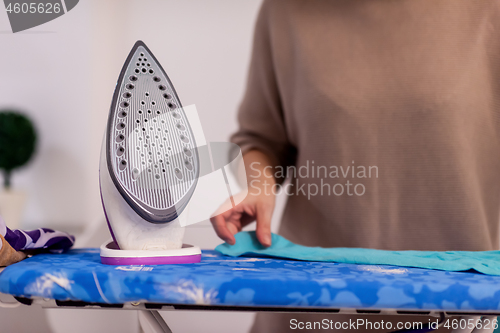 Image of Red haired woman ironing clothes at home