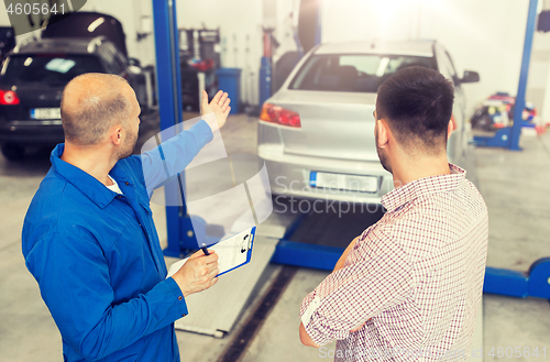 Image of auto mechanic with clipboard and man at car shop