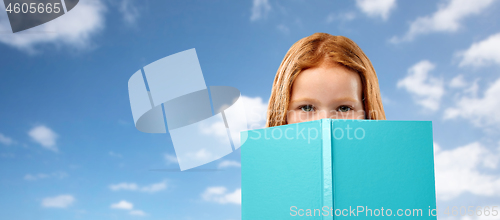 Image of red haired girl hiding behind book over sky