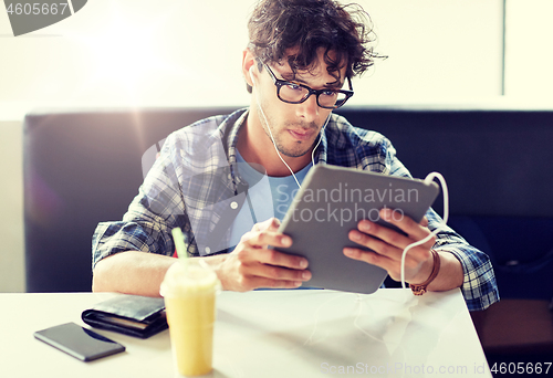 Image of man with tablet pc and earphones sitting at cafe