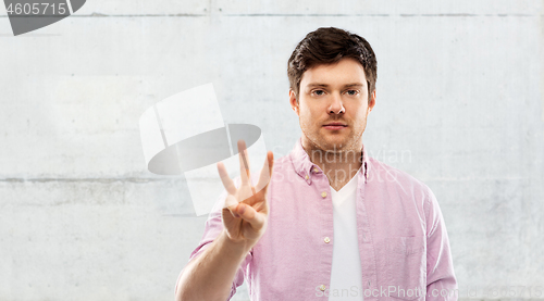 Image of young man showing three fingers over grey