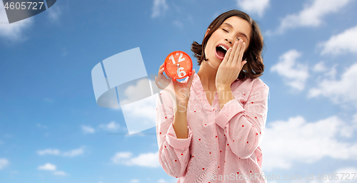 Image of sleepy woman in pajama with alarm clock yawning