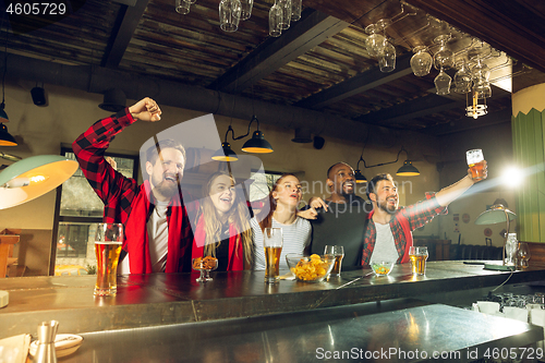 Image of Sport fans cheering at bar, pub and drinking beer while championship, competition is going