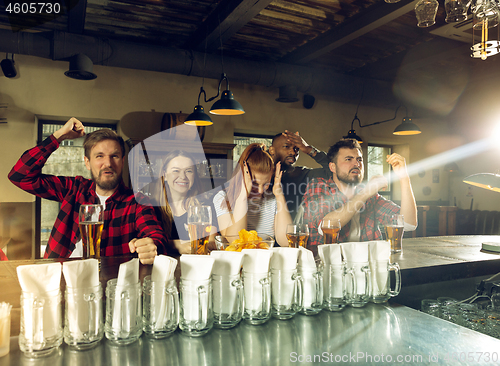 Image of Sport fans cheering at bar, pub and drinking beer while championship, competition is going