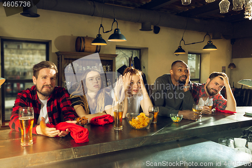 Image of Sport fans cheering at bar, pub and drinking beer while championship, competition is going