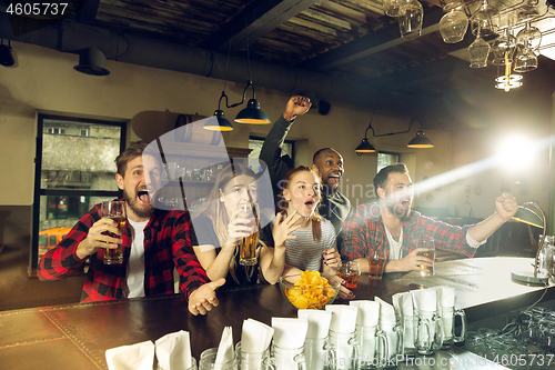 Image of Sport fans cheering at bar, pub and drinking beer while championship, competition is going