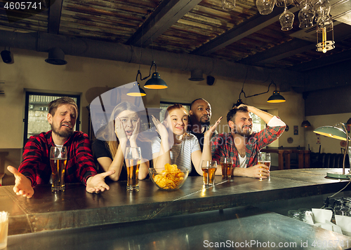 Image of Sport fans cheering at bar, pub and drinking beer while championship, competition is going
