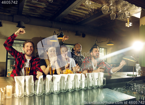 Image of Sport fans cheering at bar, pub and drinking beer while championship, competition is going