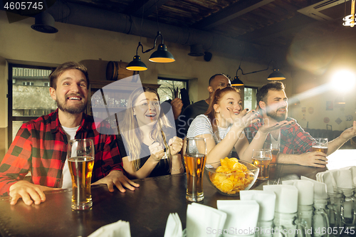 Image of Sport fans cheering at bar, pub and drinking beer while championship, competition is going