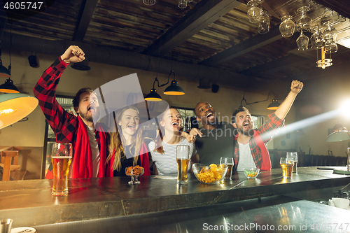 Image of Sport fans cheering at bar, pub and drinking beer while championship, competition is going