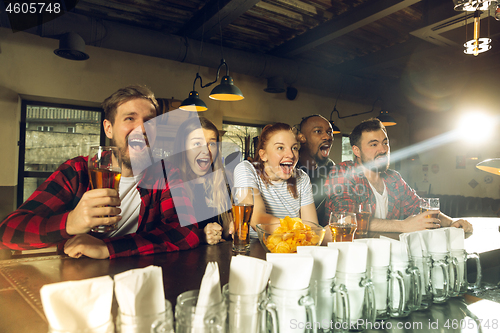 Image of Sport fans cheering at bar, pub and drinking beer while championship, competition is going