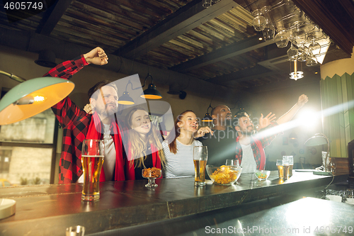 Image of Sport fans cheering at bar, pub and drinking beer while championship, competition is going