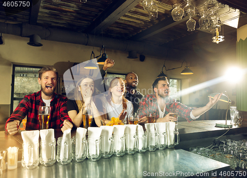 Image of Sport fans cheering at bar, pub and drinking beer while championship, competition is going