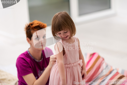 Image of young mother helping daughter while putting on a dress