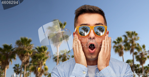 Image of surprised man in sunglasses over palm trees