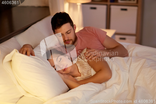 Image of man waking his sleeping wife up in bed at home