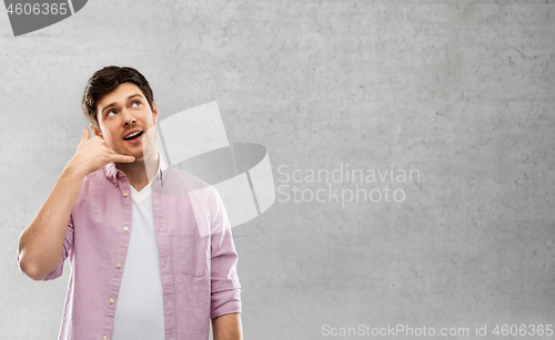 Image of man showing phone call gesture over concrete wall