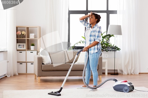 Image of tired african woman with vacuum cleaner at home