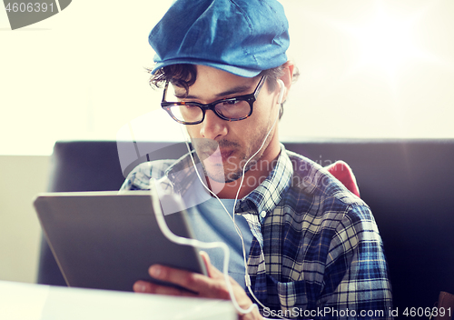 Image of man with tablet pc and earphones sitting at cafe