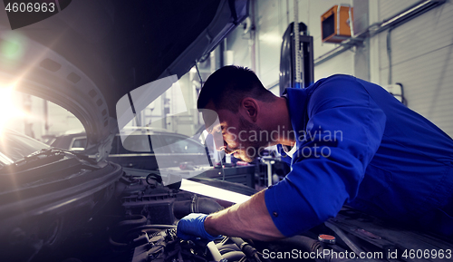 Image of mechanic man with lamp repairing car at workshop