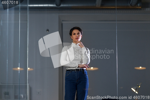 Image of businesswoman looks at glass wall at night office