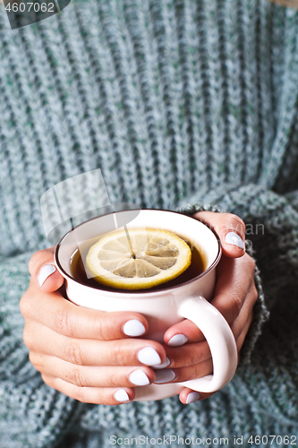 Image of Female hands holding mug of hot tea with lemon in morning. Young