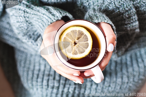 Image of Female hands holding mug of hot tea with lemon in morning. Young
