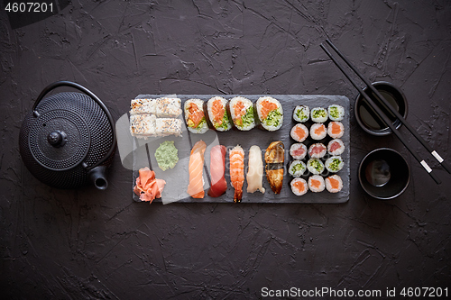 Image of Assortment of different kinds of sushi rolls placed on black stone board