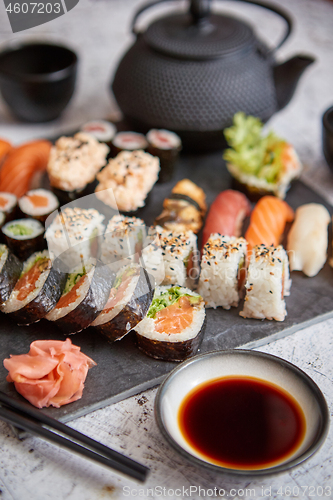 Image of Assortment of different kinds of sushi rolls placed on black stone board