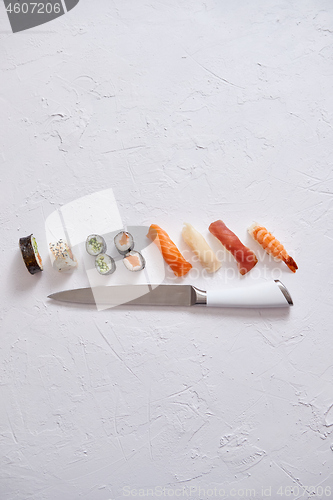 Image of Various sushi rolls with Japanese knife on white stone slate background