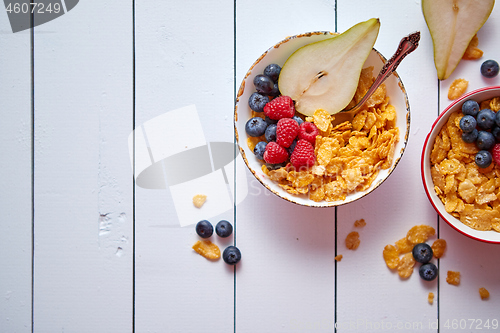 Image of Golden cornflakes with fresh fruits of raspberries, blueberries and pear in ceramic bowl