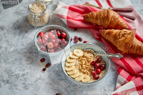 Image of Ceramic bowl of oatmeal porridge with banana, fresh cranberries and walnuts