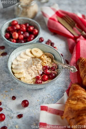 Image of Ceramic bowl of oatmeal porridge with banana, fresh cranberries and walnuts