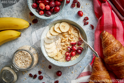 Image of Ceramic bowl of oatmeal porridge with banana, fresh cranberries and walnuts