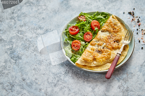 Image of Classic egg omelette served with cherry tomato and arugula salad on side
