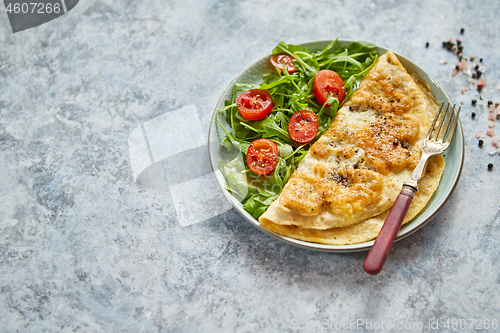 Image of Classic egg omelette served with cherry tomato and arugula salad on side