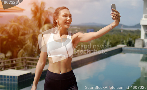 Image of Cheerful sportswoman taking selfie on poolside