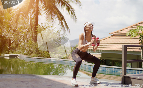 Image of Sportswoman squatting with dumbbells on poolside