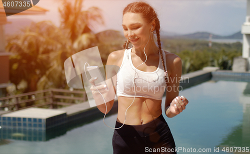 Image of Smiling sportswoman listening to music near swimming pool