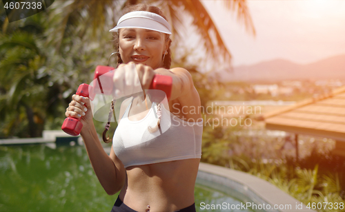 Image of Cheerful woman exercising with dumbbells near swimming pool