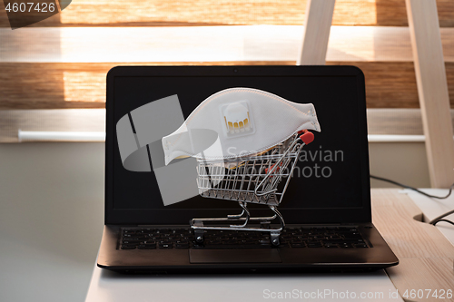 Image of Conceptual photo with miniature shopping-cart and protecting mask. Safety internet shopping
