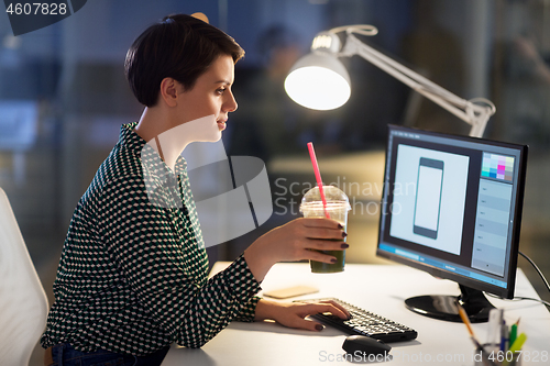 Image of designer with smoothie at computer at night office