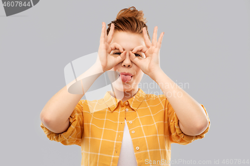 Image of red haired teenage girl making finger glasses